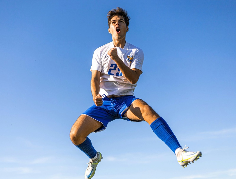 A footballer leaping in celebration against a clear sky